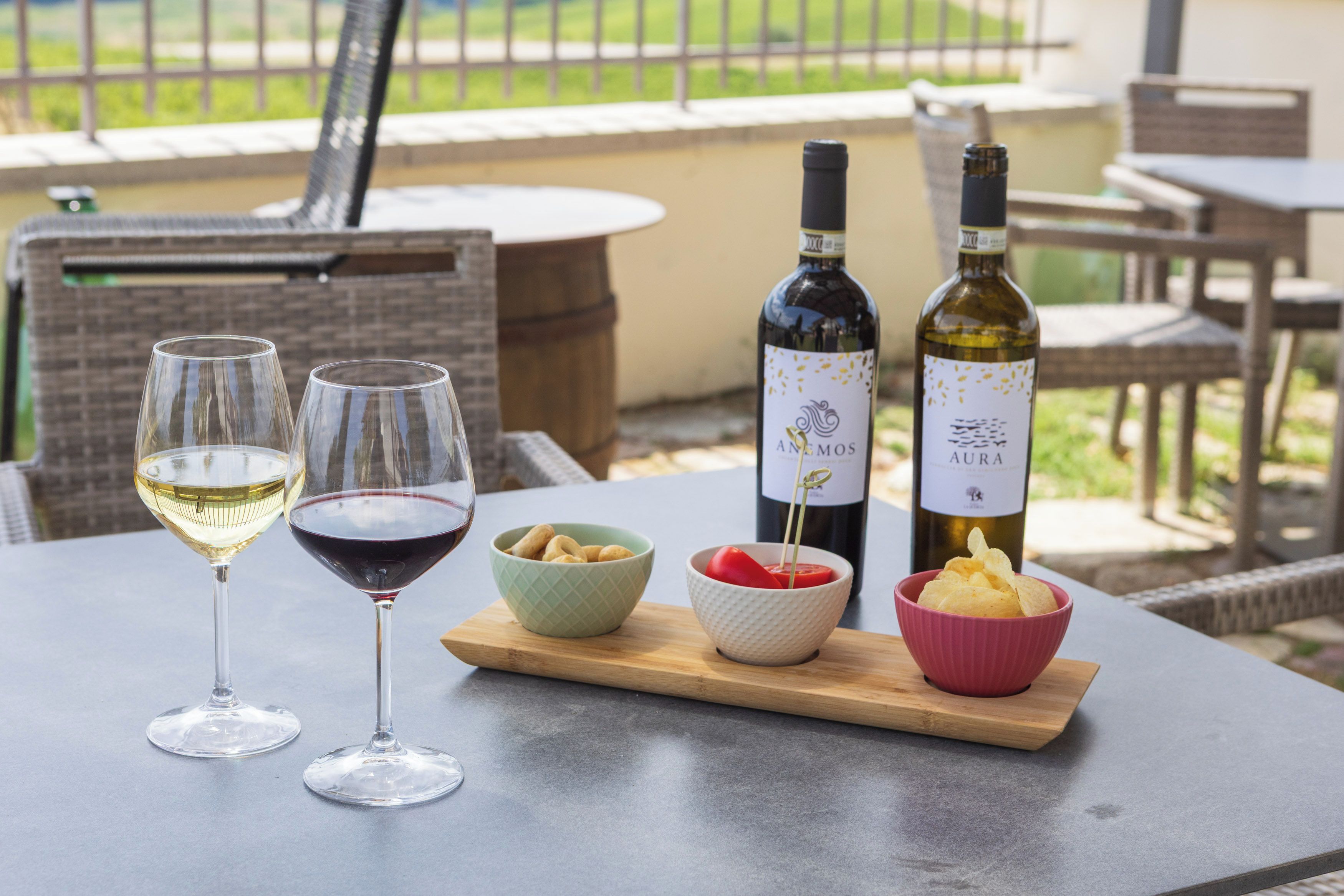 A table with two wine glasses, a bottle of wine, and bowls of snacks.