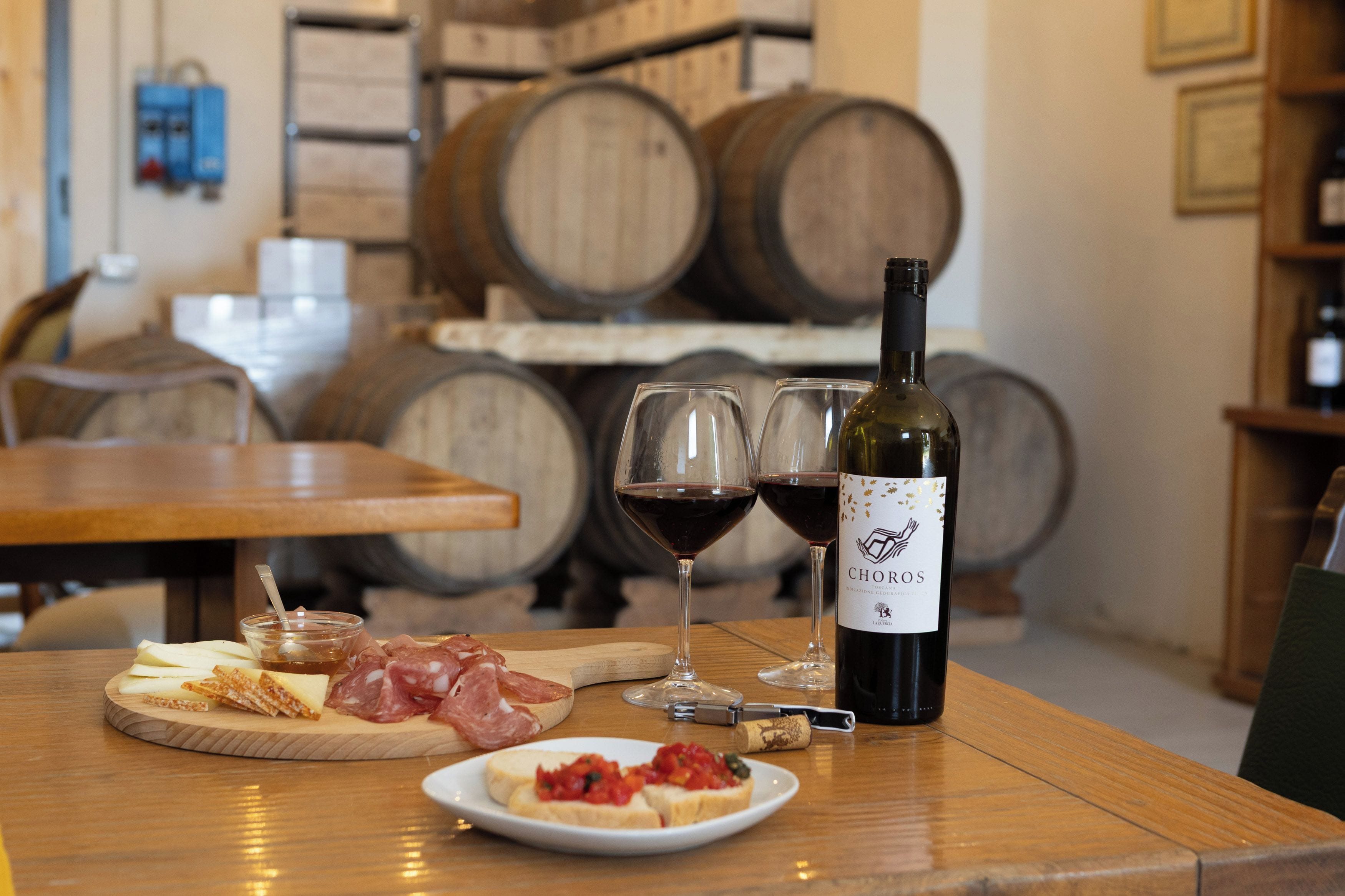 A wooden table with a bottle of wine, glasses, cheese, cured meats, and a small dish of tomato topping.
