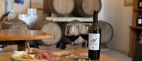 A wooden table with a bottle of wine, glasses, cheese, cured meats, and a small dish of tomato topping.