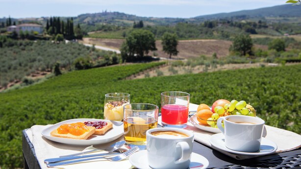 A table with breakfast items and drinks, set against a vineyard backdrop. - Podere La Quercia (San Gimignano)