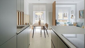 Cozinha moderna com ilha central, área de refeições com cadeiras e sala de estar com sofá e televisão.