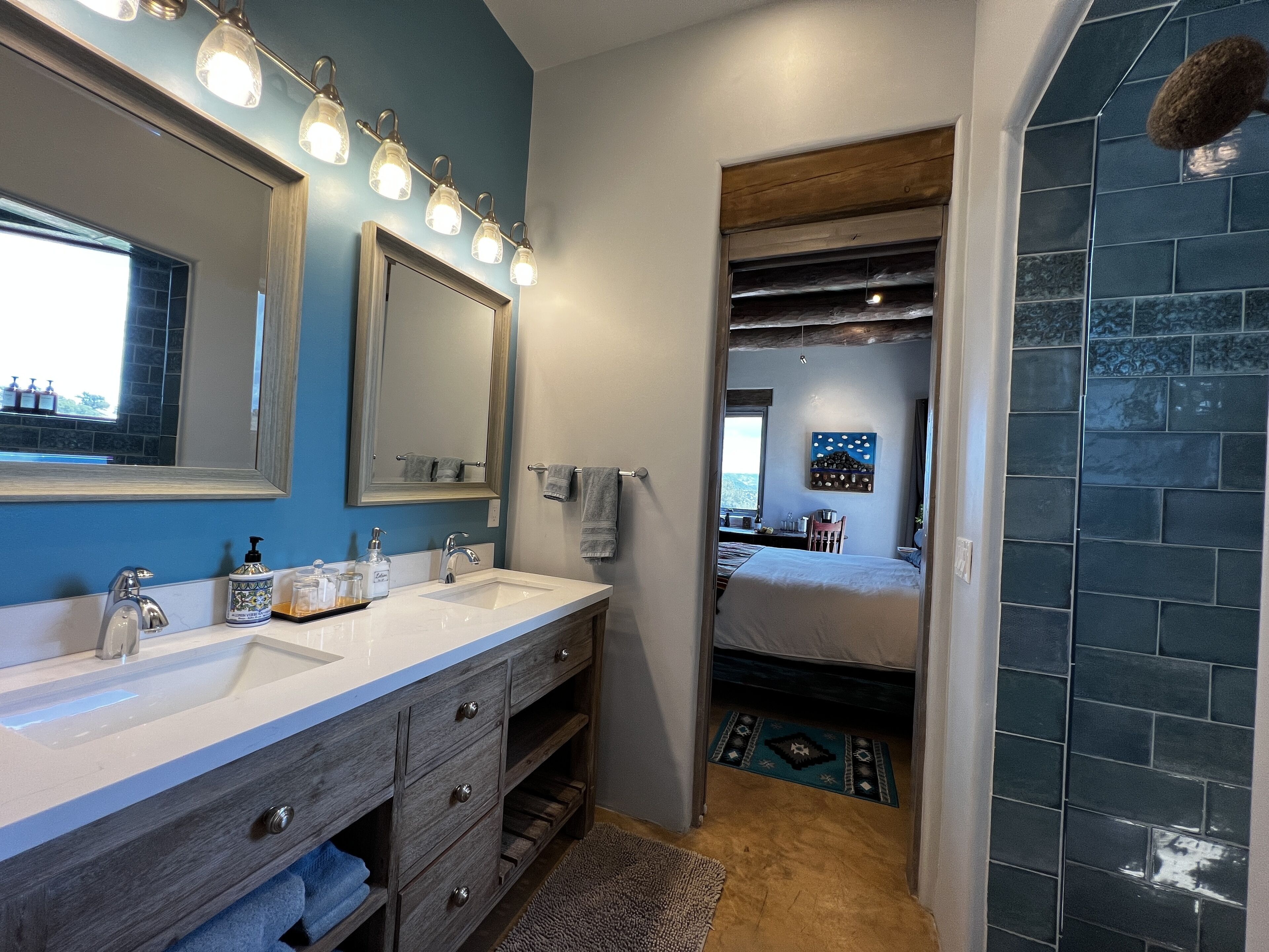 Une salle de bain dotée d’un meuble-lavabo à deux vasques, d’un grand miroir et d’un espace douche avec des carreaux de couleur foncée.