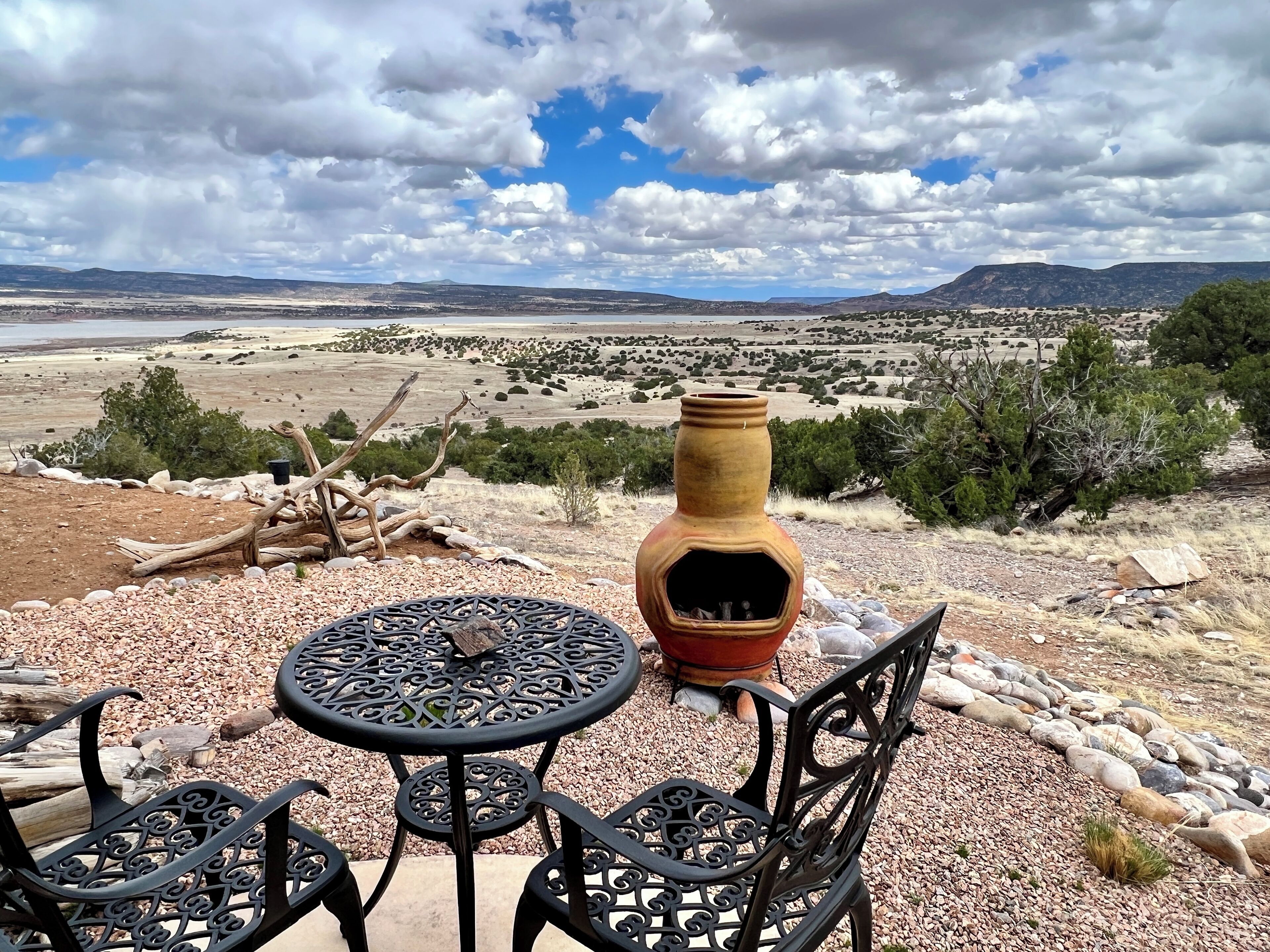 Un patio con una mesa, sillas, un jarrón decorativo y vistas a un paisaje desértico.