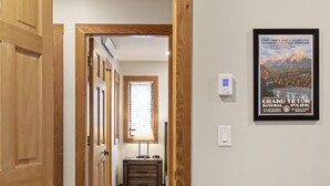 A hallway with wooden doors, a lamp, a framed picture of Grand Teton National Park, and a thermostat on the wall. - Outpost: Nez Perce C3 - Pool and Hot Tub Access! (Teton Village)