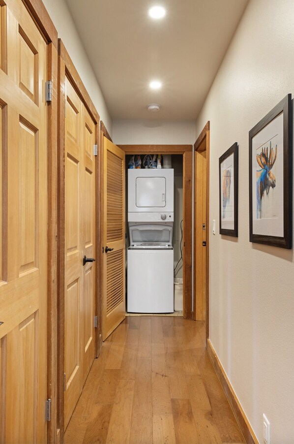 A hallway with wooden doors, a white appliance, and framed artwork on the wall.