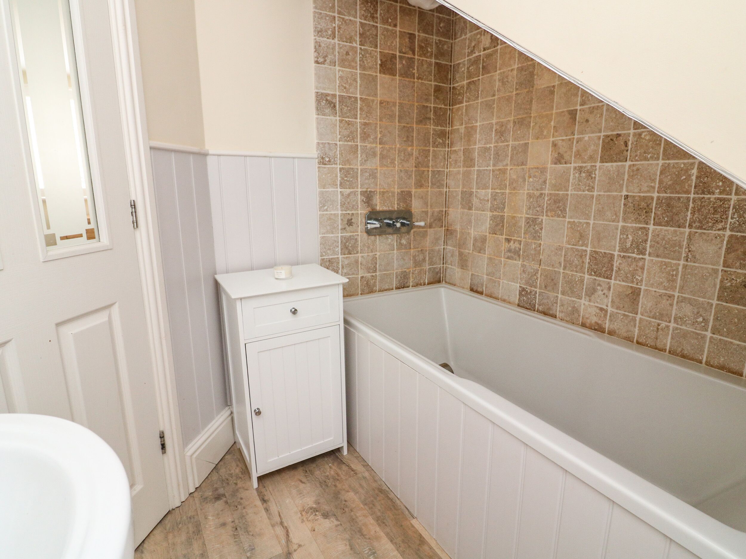 A bathroom with a white vanity, a bathtub, and a tiled shower wall.