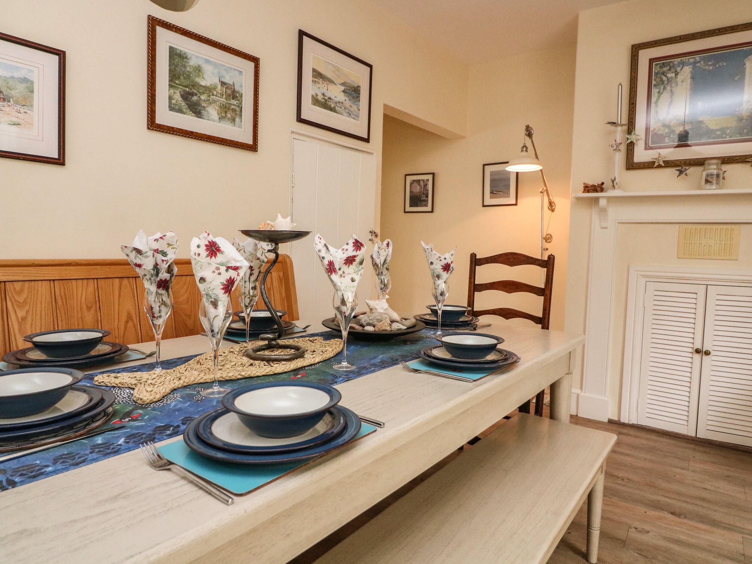A dining area with a long table set for a meal, framed artwork on the walls, and a fireplace with a mirror.