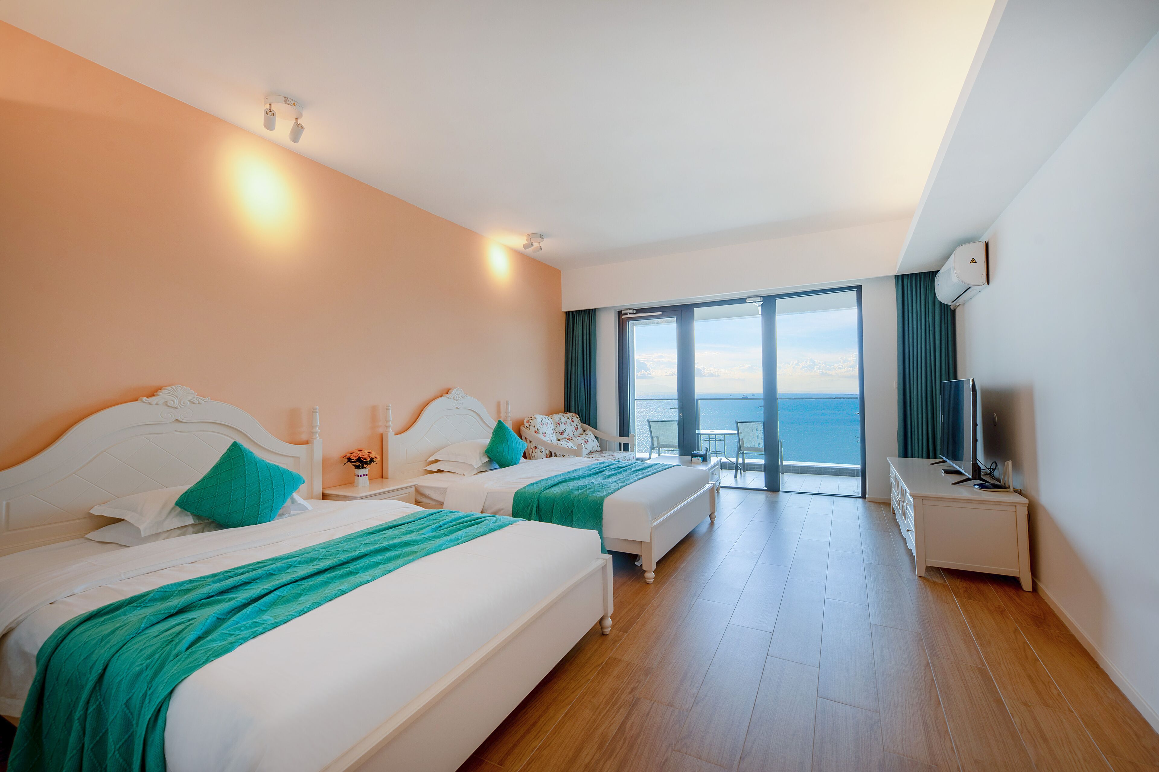 A hotel room with two beds, a desk, and a large window offering a view of the sea.