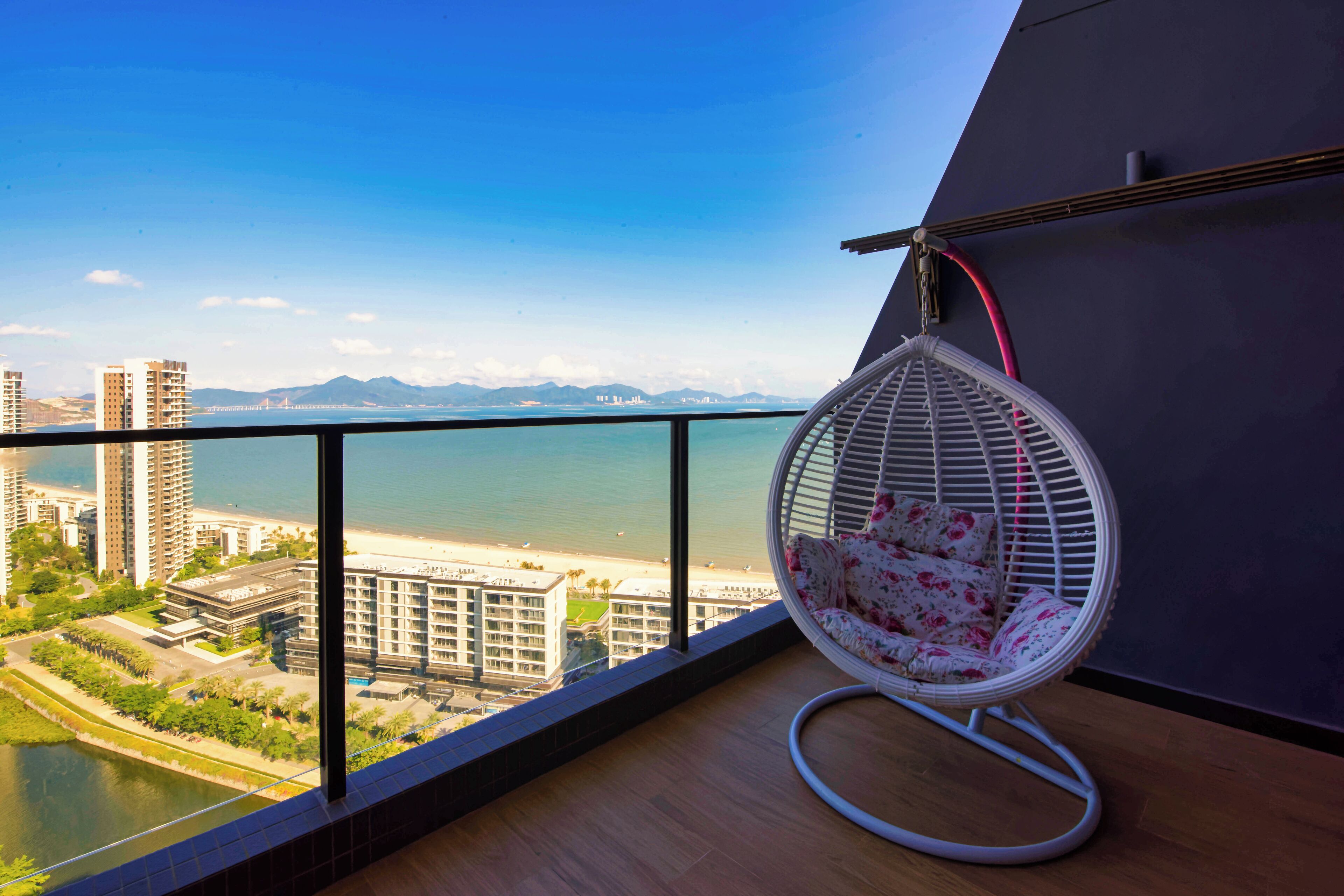 Ein Balkon mit Blick auf Strand und Stadtbild, ein Hängestuhl und ein Holzboden.