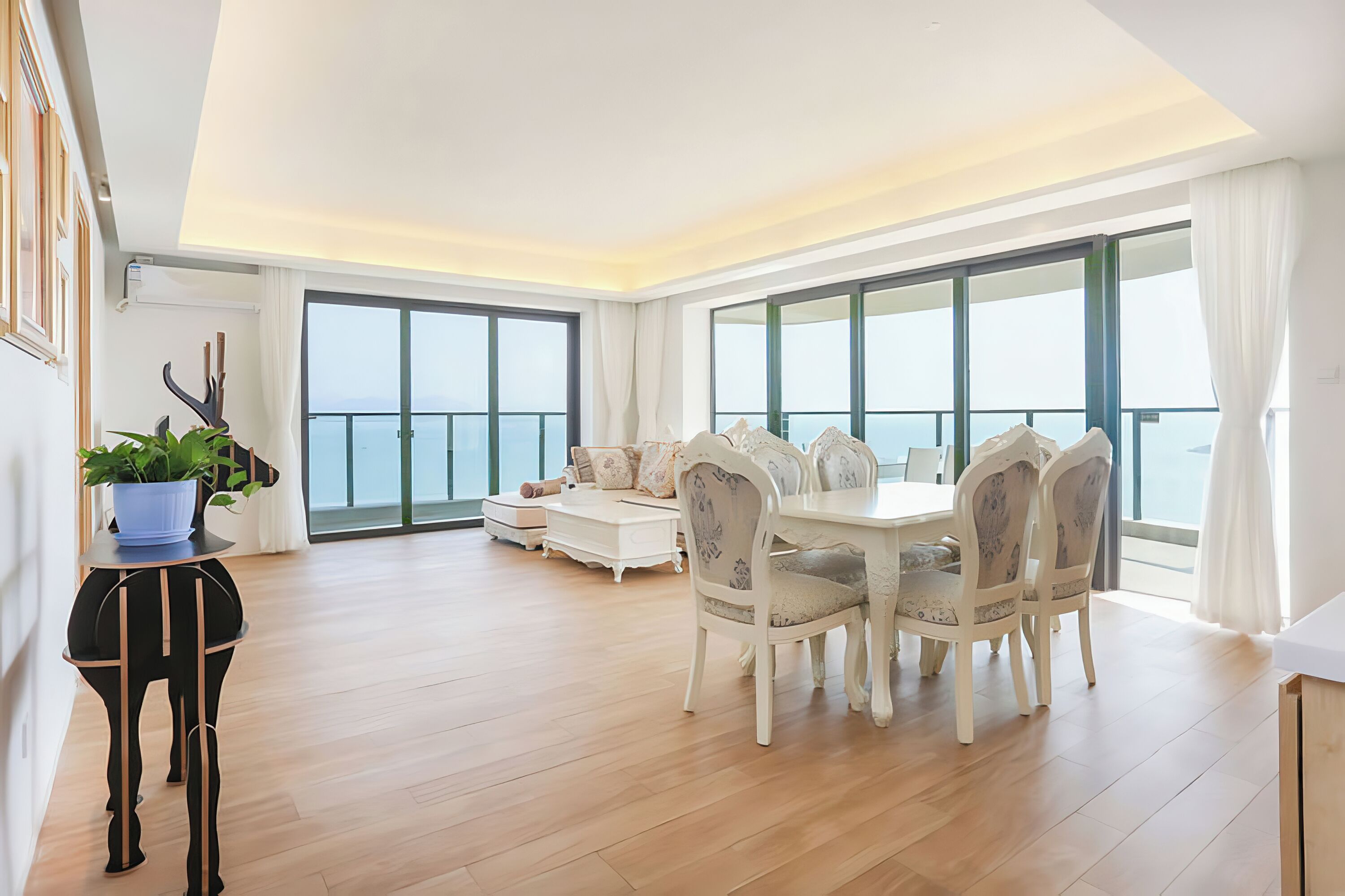 Amplia sala de estar con mesa y sillas de comedor, un sofá y un ventanal con vista al mar.