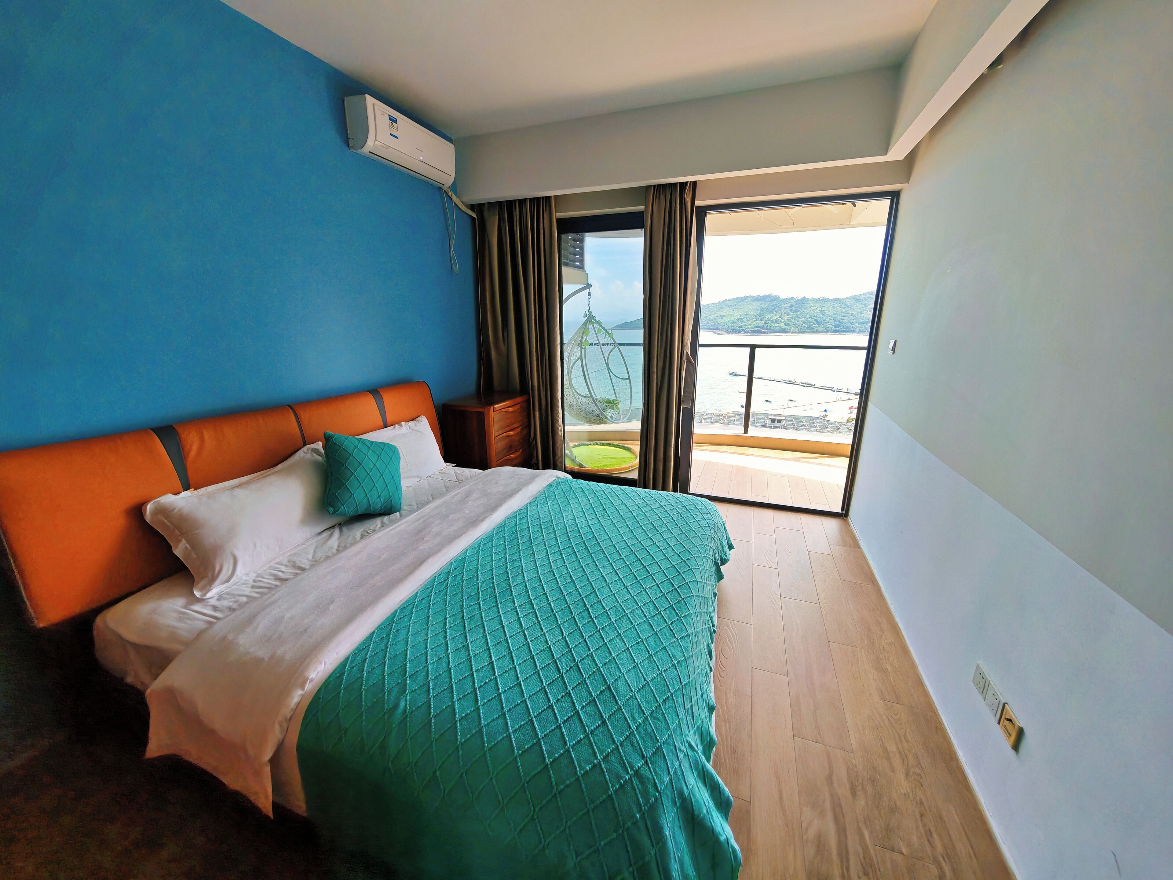 Ein Schlafzimmer mit einem Bett, einem Nachttisch und Blick auf einen Balkon mit Geländer.