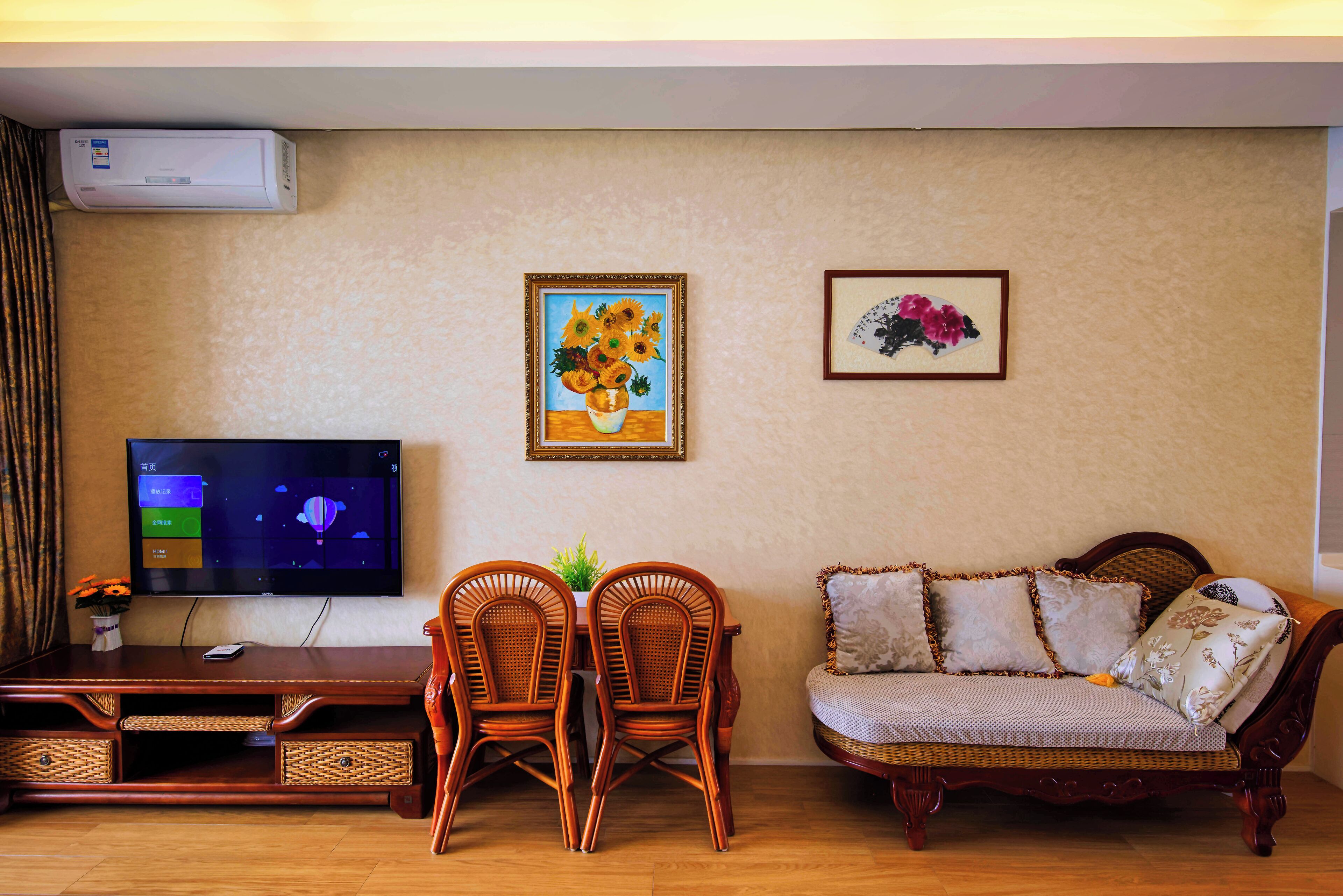 Uma sala de estar com televisão, duas cadeiras de vime, um sofá e dois quadros pendurados na parede.