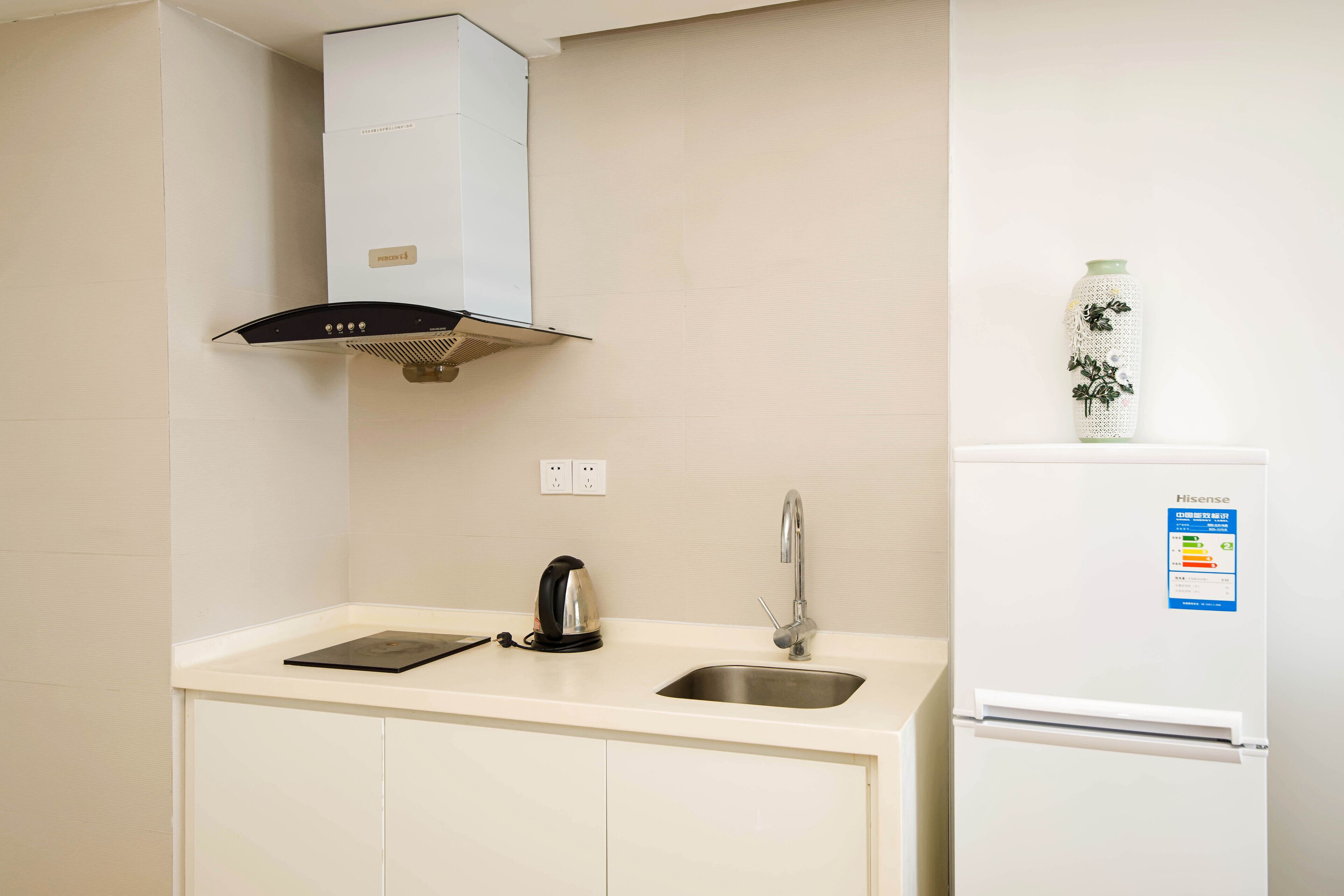 Una kitchenette compacta equipada con estufa, tetera, lavamanos y refrigerador.
