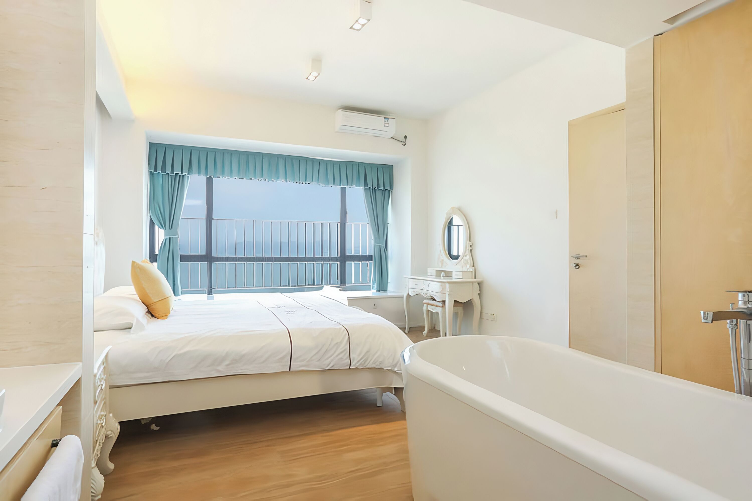 Ein Schlafzimmer mit einem großen Bett, einem Fenster mit Vorhängen, einem Schminktisch mit Spiegel und einer Badewanne.