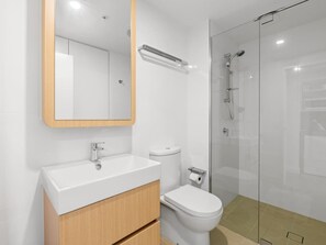 A modern bathroom with a white sink, wooden vanity, a toilet, and a glass-enclosed shower area.