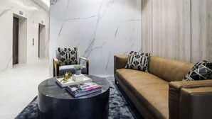 En modern hotellobby med en vägg av marmor, en soffa klädd i läder och ett runt soffbord.