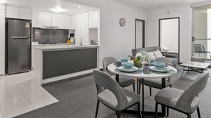 Una cucina moderna con mobili bianchi, un frigorifero in acciaio inossidabile e un'area pranzo con un tavolo rotondo e sedie grigie.