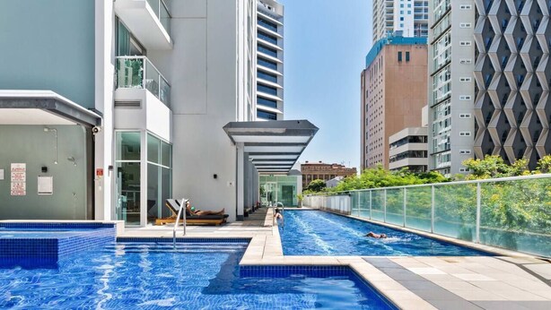 Una piscina interna con acqua cristallina e limpida, circondata da edifici moderni e una ringhiera in vetro.