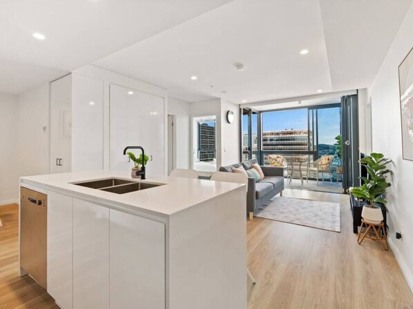 A modern kitchen with a central island, a dining area with a sofa and chairs, and a large window offering a city view.