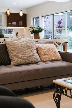 A modern living room with a sofa, decorative pillows, a glass-top coffee table, and pendant lighting.