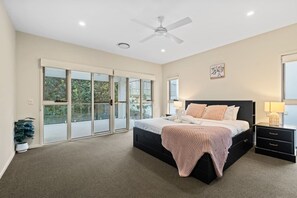 A bedroom with a bed, a nightstand, a lamp, a ceiling fan, and a sliding glass door leading to a balcony.
