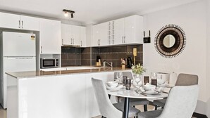 Eine moderne Küche mit weißen Schränken, einer zentralen Kochinsel und einem Essbereich mit weißem Tisch und grauen Stühlen.