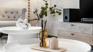 Ein modernes Wohnzimmer mit einem weißen runden Couchtisch, einem weißen Dekorationsgegenstand und einer Vase mit gelben und schwarzen Akzenten.