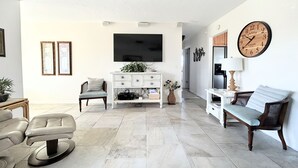 Uma sala de estar com televisão, sofá, poltrona, mesa de centro e relógio na parede.