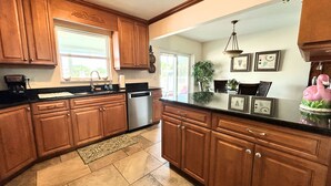 A kitchen with wooden cabinets, a stainless steel dishwasher, a black countertop, and a decorative flamingo. - Pets, Plunges & Peace on the Gulf of Mexico (Nokomis)
