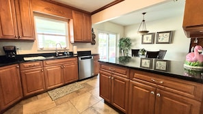 A kitchen with wooden cabinets, a stainless steel dishwasher, a black countertop, and a decorative flamingo. - Pets, Plunges & Peace on the Gulf of Mexico (Nokomis)