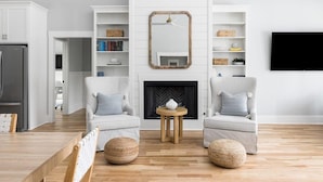 A modern living room with two armchairs, a fireplace, and built-in shelving with books and decorative items. - Jungle House-Heated Pool-Pet Friendly-Luxury (Edisto Island)