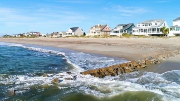 A beachfront property with houses along the shore, a rocky shoreline, and waves crashing onto the beach. - Jungle House-Heated Pool-Pet Friendly-Luxury (Edisto Island)