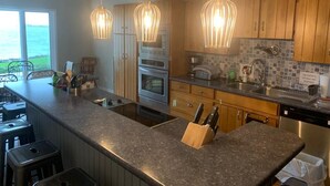 Een keuken met granieten aanrechtbladen, houten kastjes, een inbouwoven en hanglampen.