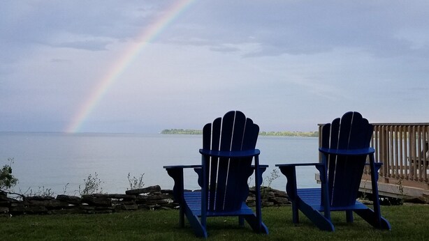 Twee Adirondack-stoelen gericht op een meer, met een regenboog.