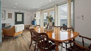 A dining area with a wooden table and chairs, a chandelier, and large windows with curtains. - Long Point Lake House - Daphne's House (Aurora)