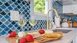 A kitchen counter with a fruit platter, two glasses of white wine, and a decorative backsplash. - Long Point Lake House - Daphne's House (Aurora)