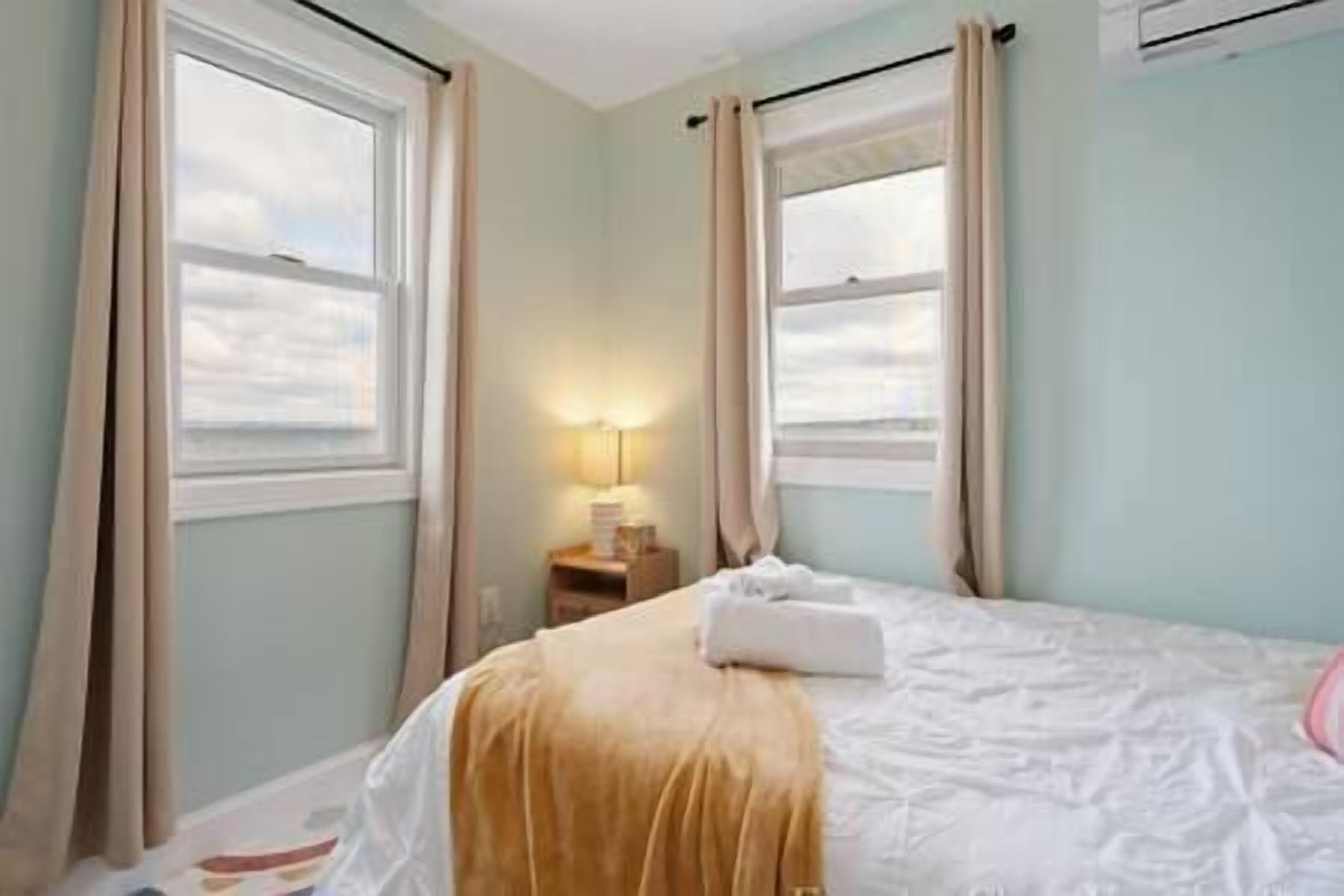 Un dormitorio con cama, cortinas, mesita de noche y lámpara.