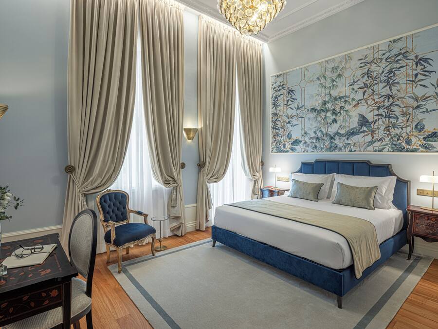 Un dormitorio con una cama grande, un escritorio con silla, un florero con flores y un cuadro en la pared.
