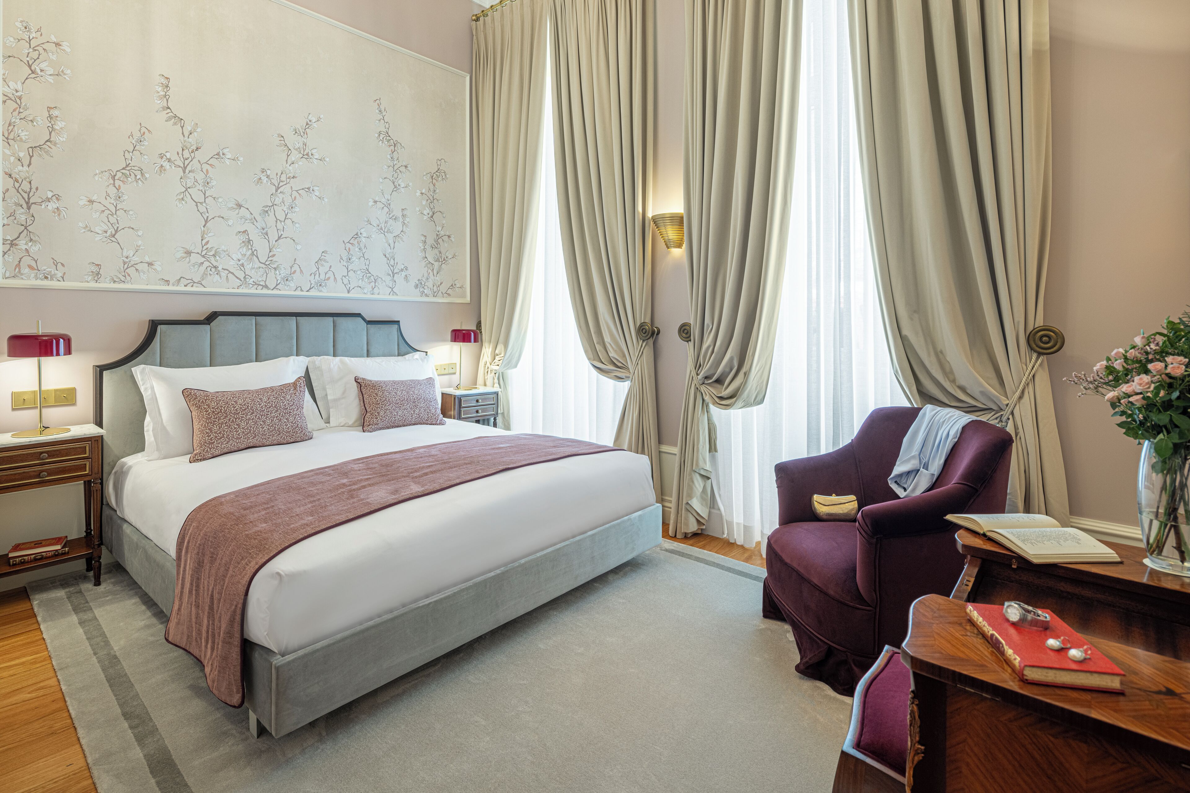 A neatly arranged bedroom with a bed, a chair, a nightstand, and a bedside table.