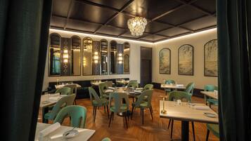Un restaurante con mesas redondas y sillas verdes, pisos de madera y espejos decorativos.