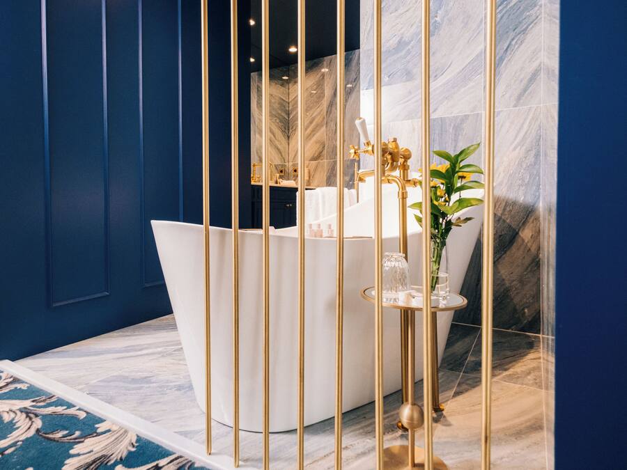 Un baño moderno con pared de mármol, bañera blanca y detalles dorados.