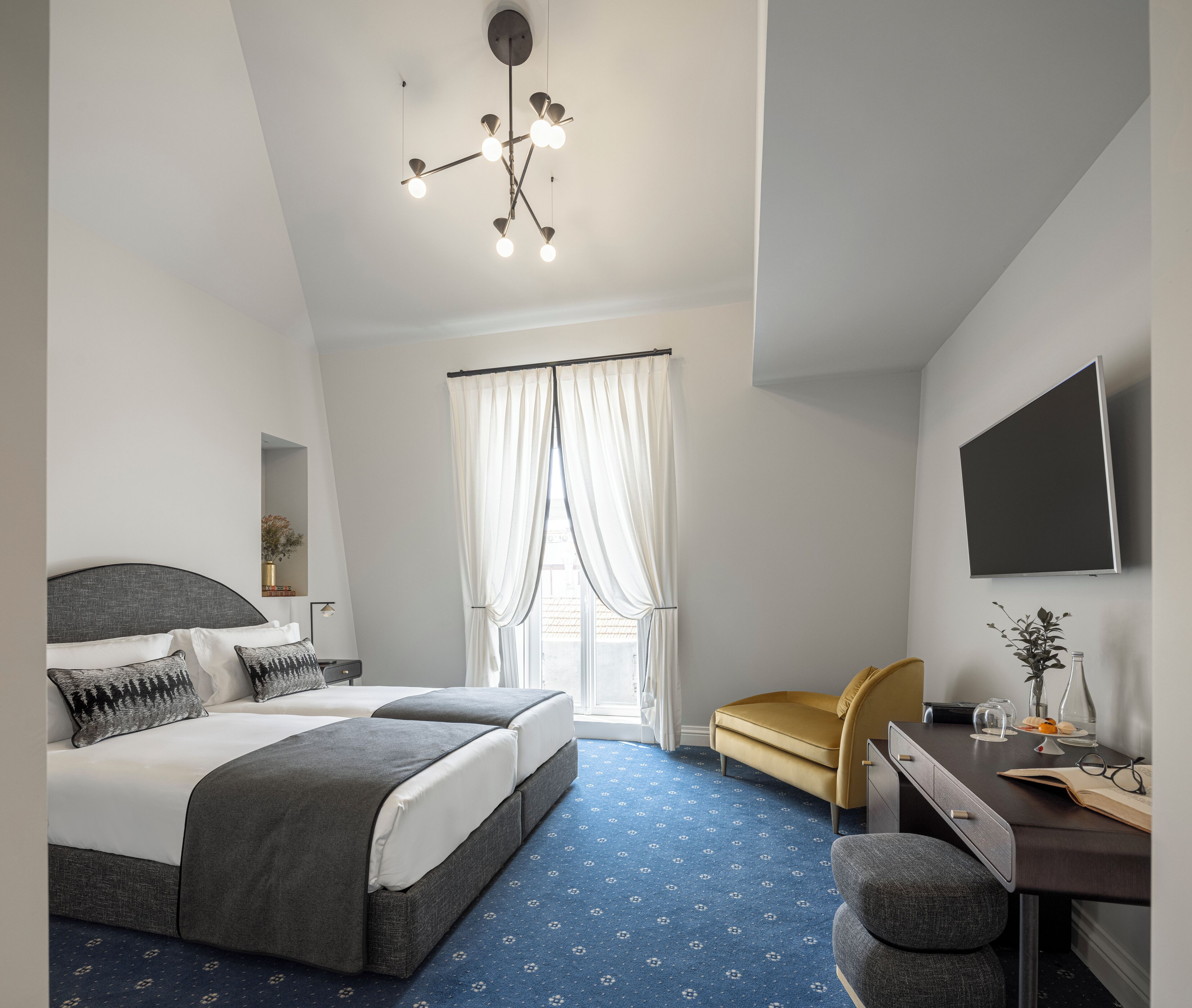 Una habitación de hotel moderna con una cama grande, un escritorio con una silla, un televisor de pantalla plana y una lámpara en el techo.