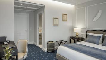 Habitación de hotel con cama, escritorio con una computadora portátil, silla, maleta y cuadros en la pared.