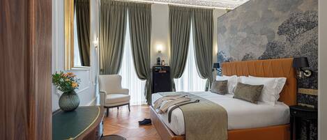 A bedroom with a large bed, a desk, a chair, and a large window with curtains.