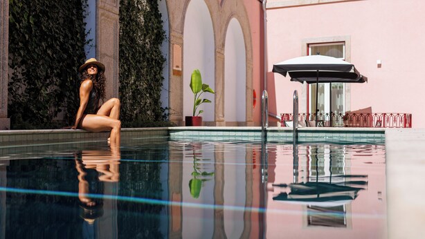 A pool area with a person sitting by the pool, a potted plant, and a red railing.