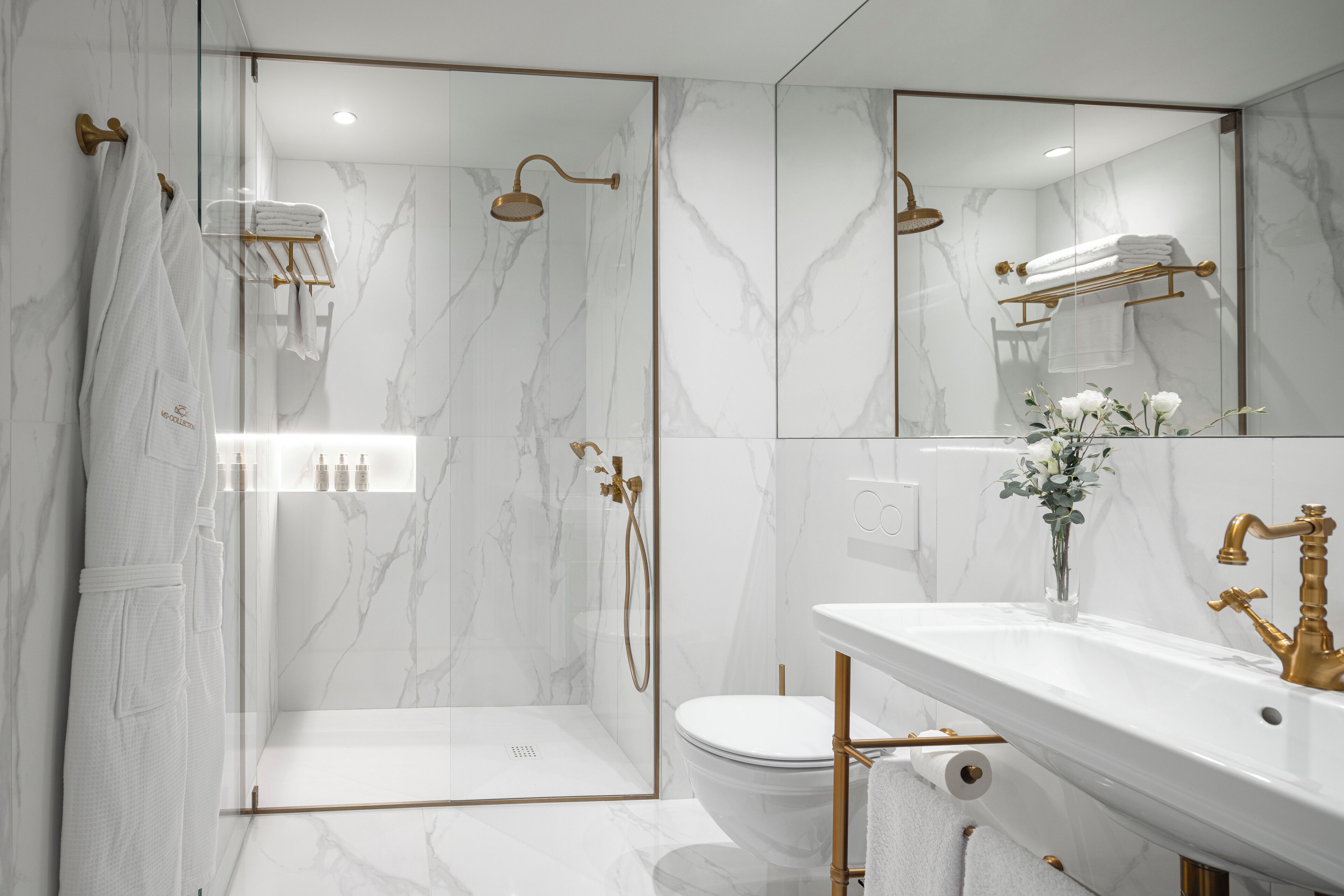 Un baño moderno con ducha acristalada, inodoro blanco y tocador con grifo dorado.