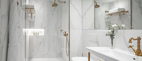 Un baño moderno con ducha acristalada, inodoro blanco y tocador con grifo dorado.