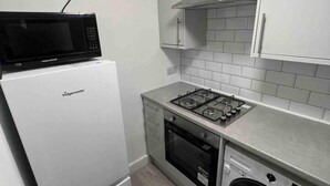 A compact kitchen with a white refrigerator, a microwave, a gas stove, an oven, and a built-in washing machine. - Spacious Luxury 2 Bedroom Apartment, Station 1min (London)