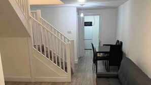 A modern living room with a staircase, a gray sofa, and a dining area with a table and chairs. - Spacious Luxury 2 Bedroom Apartment, Station 1min (London)