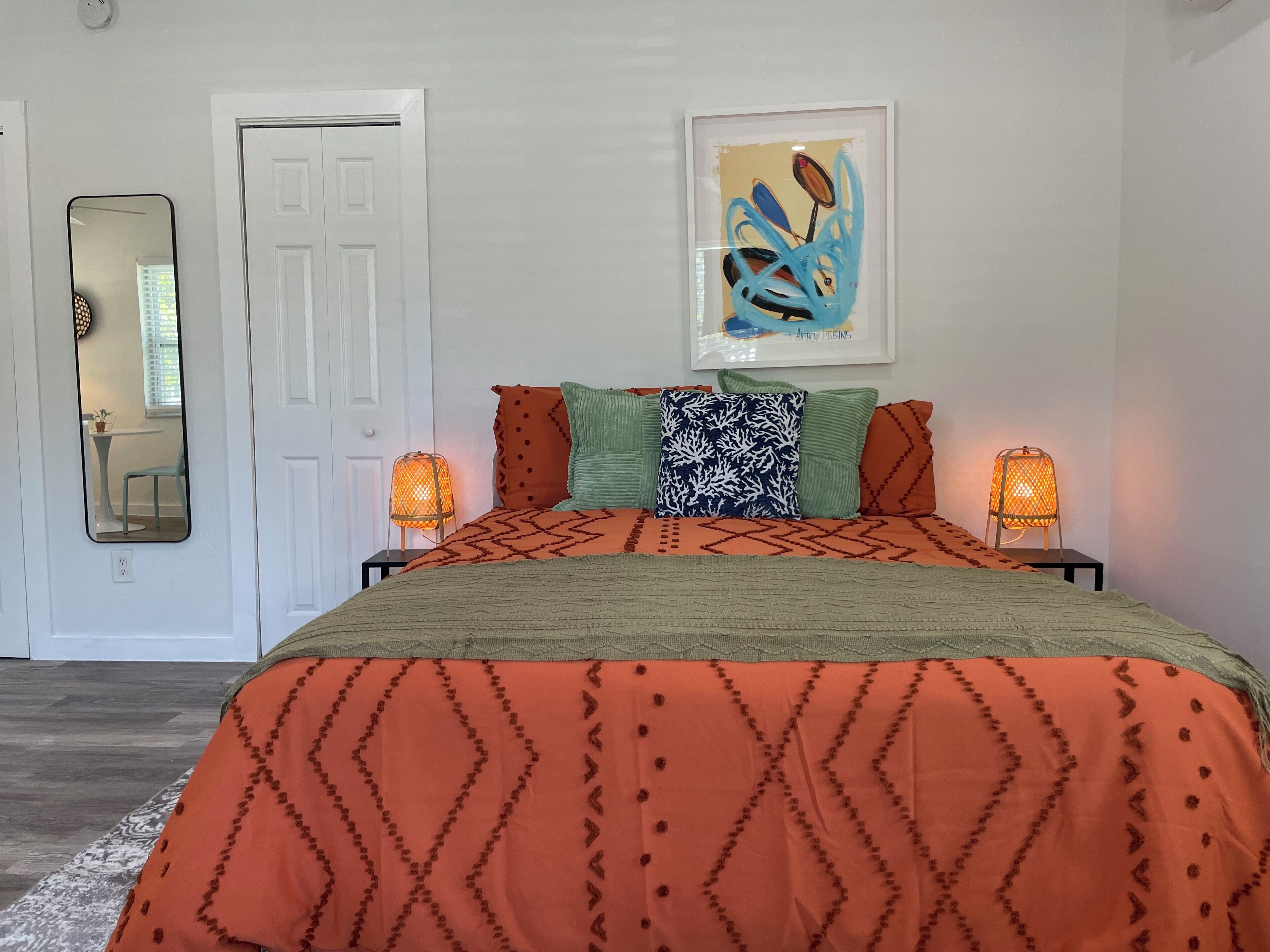 A bedroom with a bed, two bedside lamps, a framed artwork, and a door.